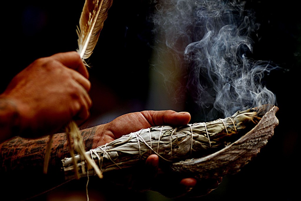 A close-up of smudging, which involves the burning of one or more medicines such as tobacco, sage, cedar or sweetgrass. A feather is used to fan the smoke from the medicine bundle.