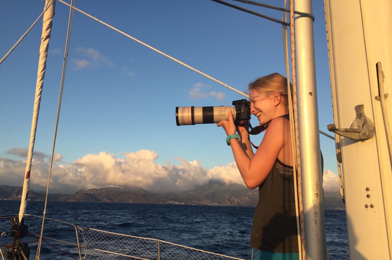 A person with long blonde hair using a telephoto lens camera on a ship in the ocean.
