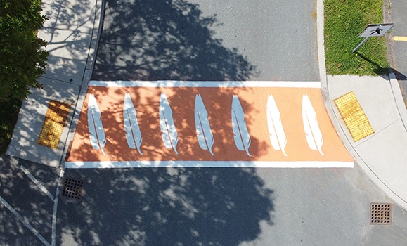 An aerial shot of an orange crosswalk with seven white feathers.