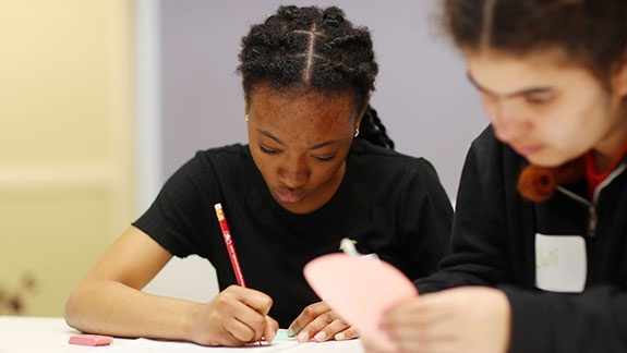 Two students are sitting at a desk doing work.