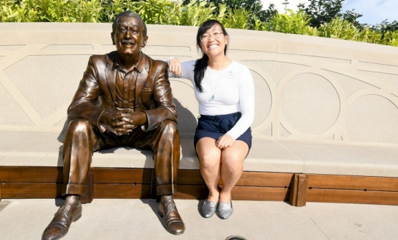 Dal alum Flo Park is sitting on a park bench with her elbow resting on a bronzed statue of Walt DIsney.