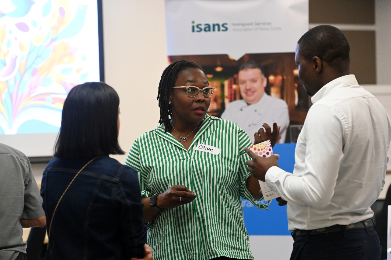 Three people talking to each other. An ISANS pull-up banner is blurred in the background.