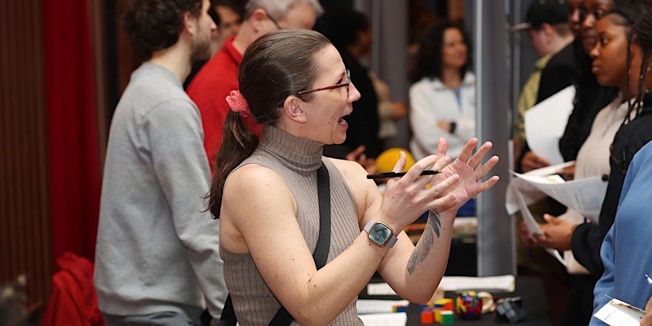A female-presenting person using their hands to explain topics to visitors at an event booth.
