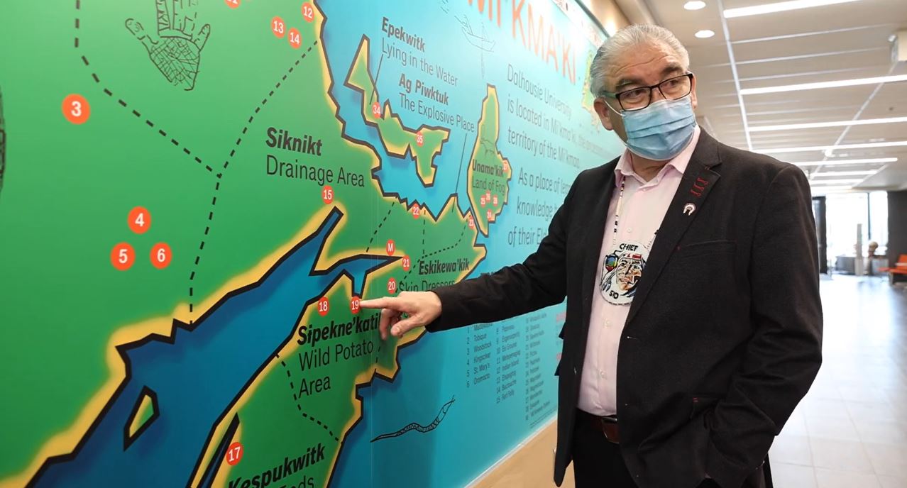 Chief Peters is pointing to a place on a large mural map of Nova Scotia.