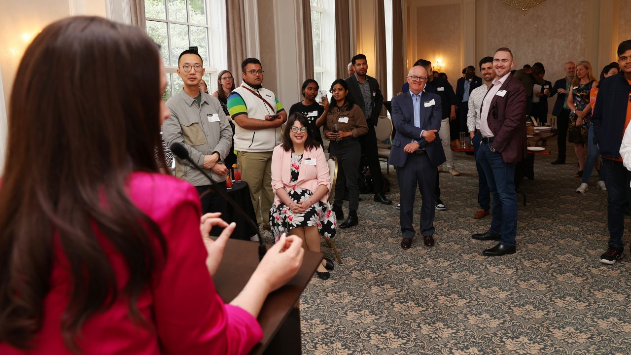A person standing in front of a group of people speaking to them at an event.