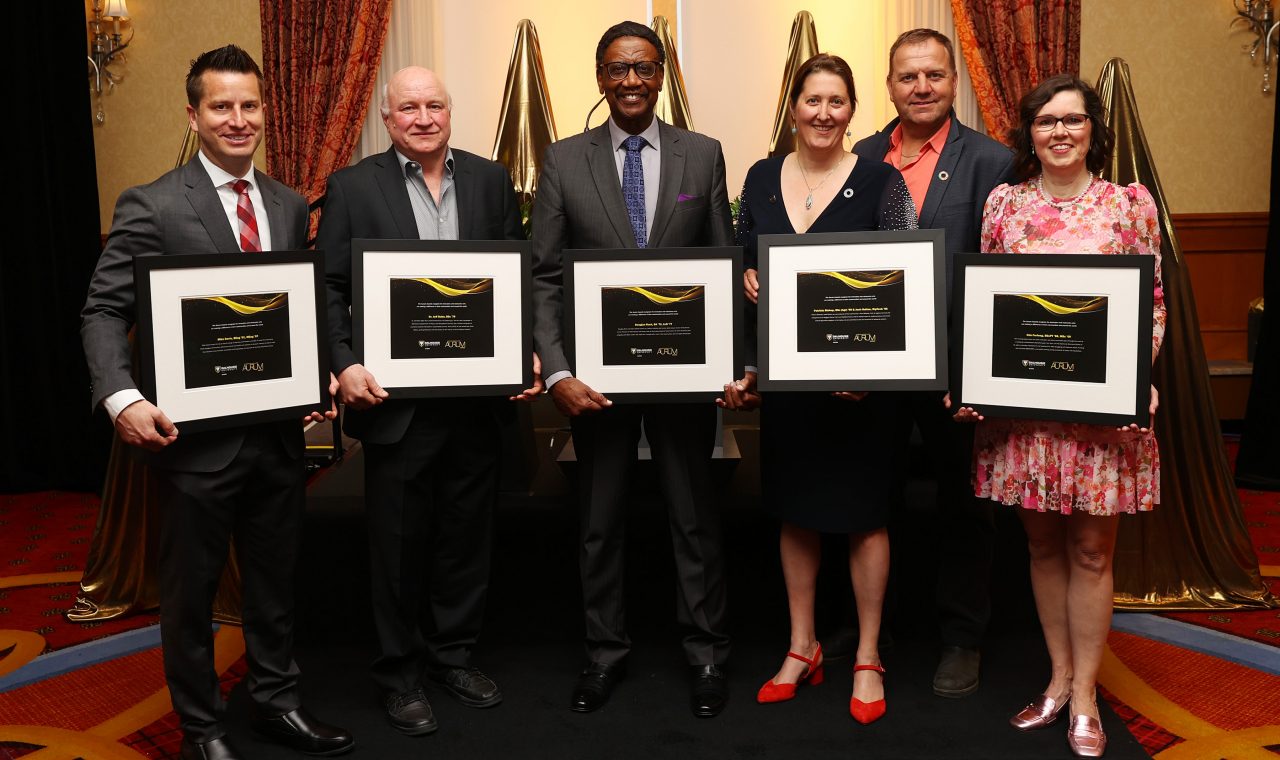 Six people pose with framed certificates at a semi-formal event.