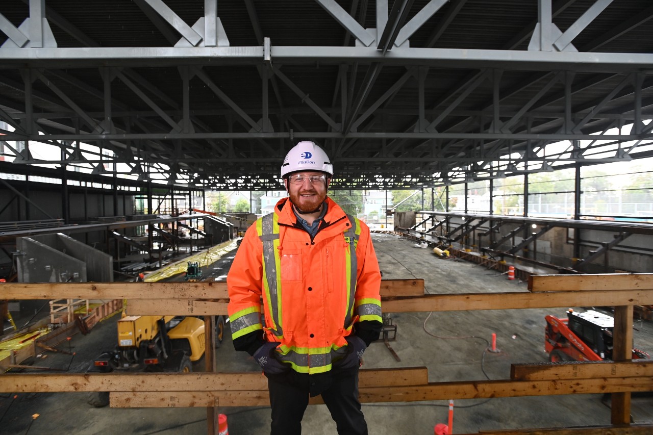 Barrett standing, smiling from an upper level under the roof of the construction site of the centre.