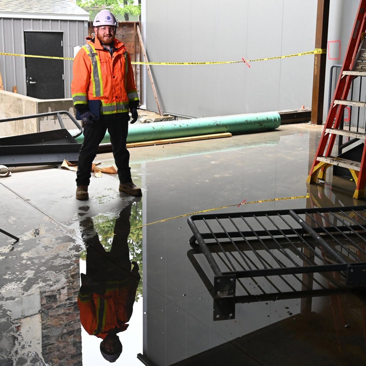 Barrett standing under the structure of the construction site, his reflection showing on the wet floor.