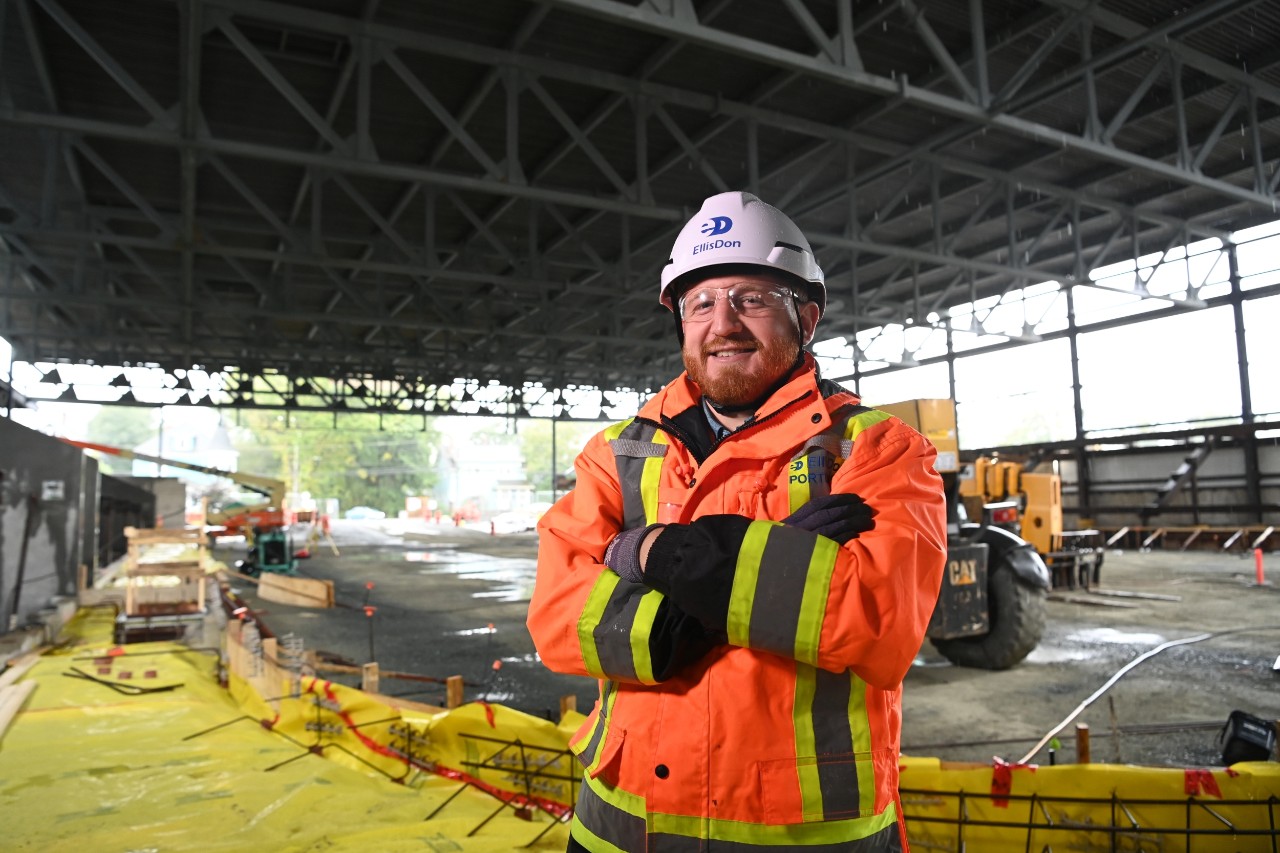 Barrett standing with arms crossed, smiling under the roof of the construction site of the centre.