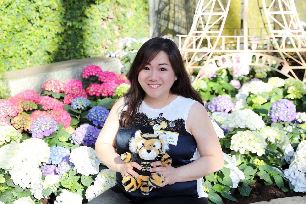 Choi-Cheung posing with a Dal Tiger stuffed animal in front of flowers. 