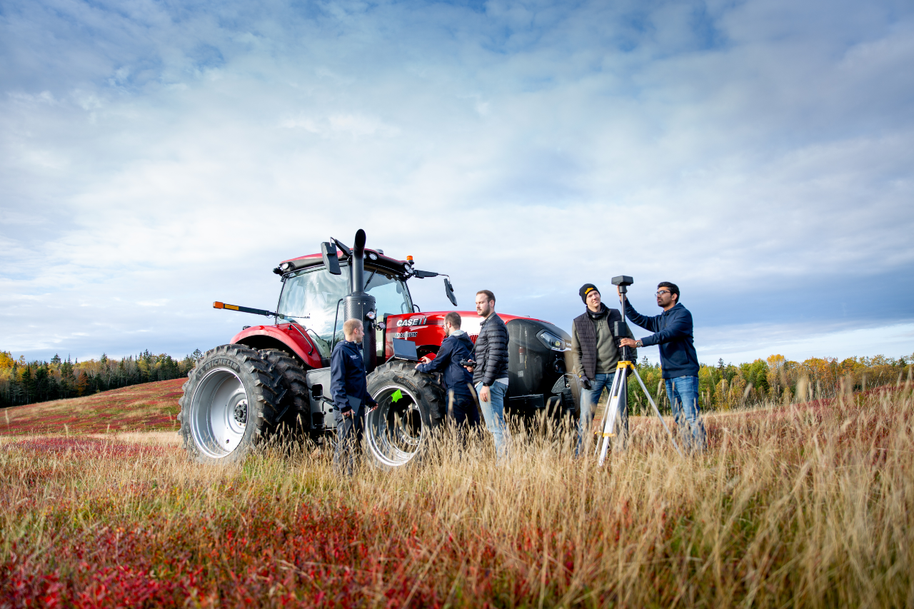 A group of students setting up equipment around a red tractor in a field