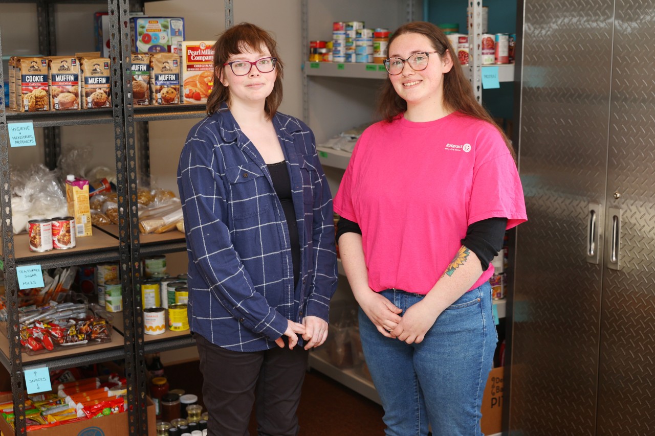 Two women with brown hair and glasses stand in a food pantry