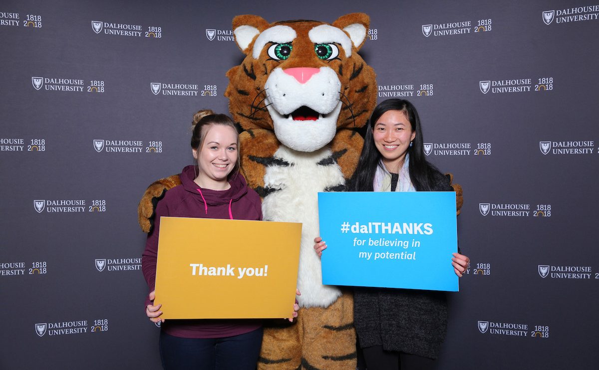 Two women holding signs that day thank you pose with the tiger mascot