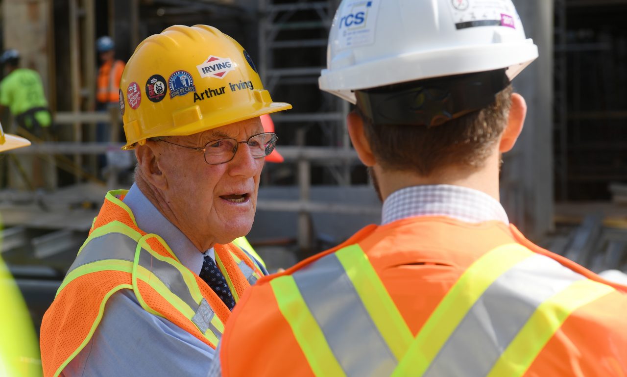 A man wearing a hard had and safety vest talks to another man in a hard hat and safety vest