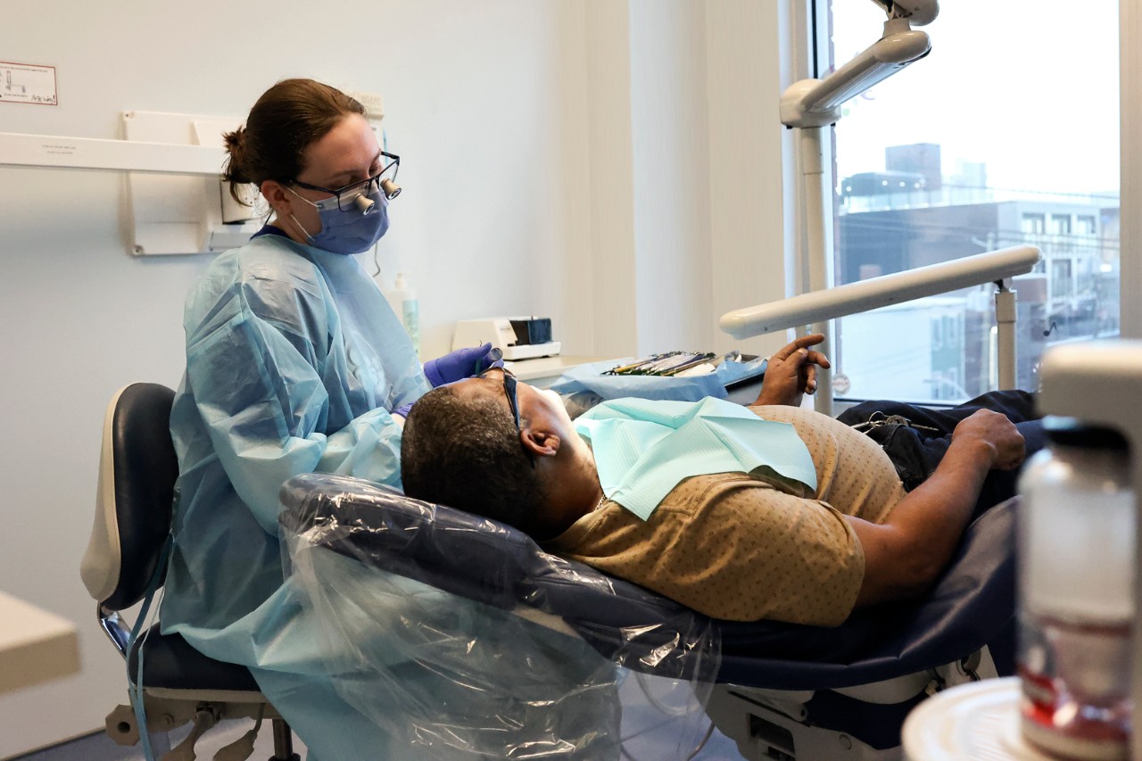 A dentist wearing a blue mask and scrubs with a patient laying in a dental chair